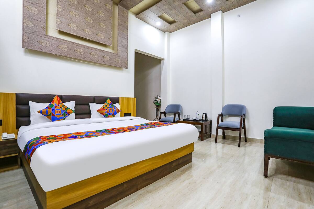 Une chambre d’hôtel avec un grand lit, deux chaises, une petite table et un panneau décoratif au mur.