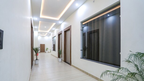 A hallway with a light-colored floor, potted plants, and doors with curtains. - Fabhotel Jb Square Resort (Faizabad)