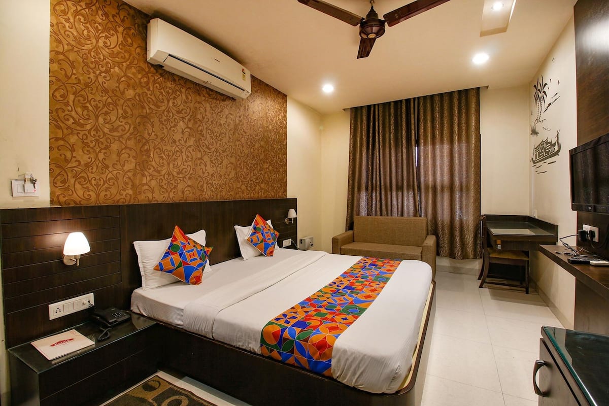 A hotel room with a large bed, a desk, a chair, an air conditioner, a ceiling fan, and a TV.