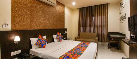 A hotel room with a large bed, a desk, a chair, an air conditioner, a ceiling fan, and a TV.