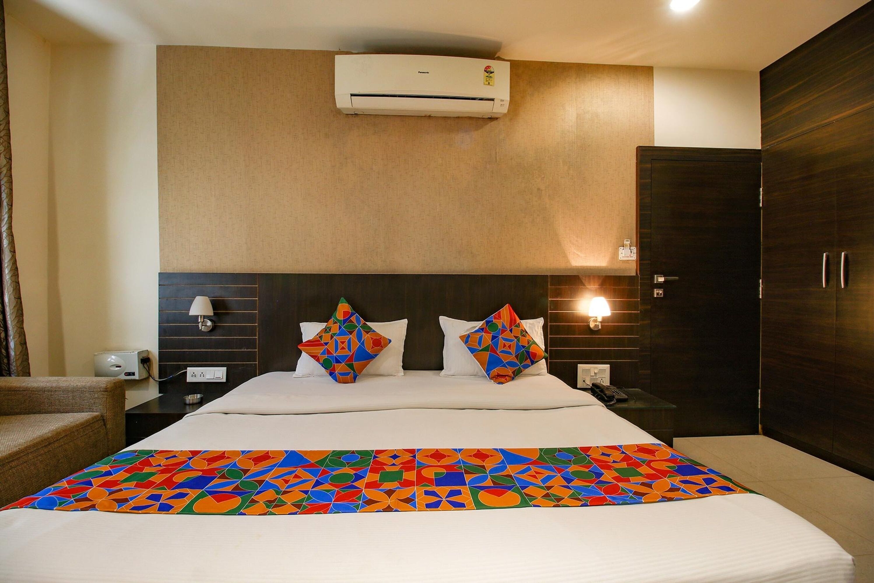 A hotel room with a bed, a nightstand, a lamp, an air conditioner, and a wardrobe.