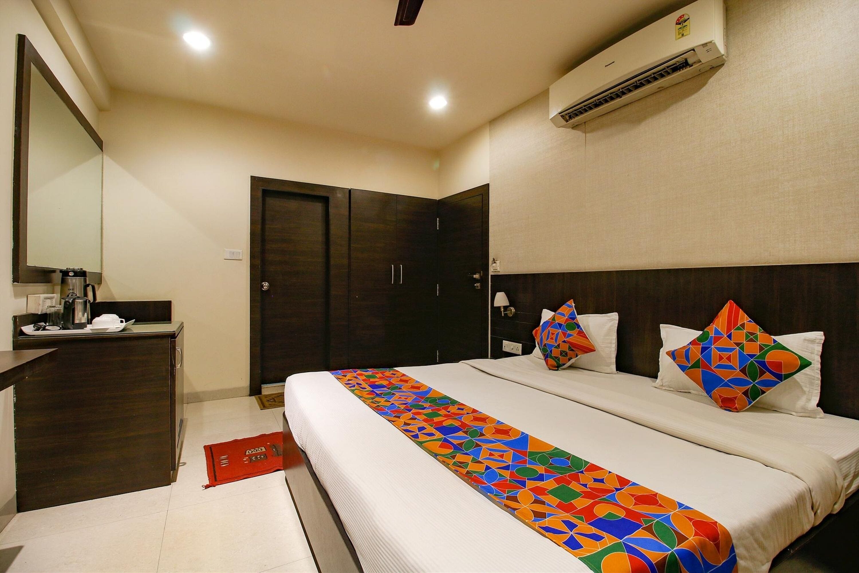 A hotel room with a large bed, a desk, a wardrobe, and an air conditioning unit.