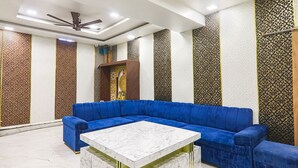 A modern living room with a blue sectional sofa, a marble coffee table, and patterned walls. - Fabhotel Keshri Inn (Prayagraj)