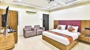 A modern hotel room with a large bed, two armchairs, a desk with a chair, a ceiling fan, and an air conditioning unit. - Fabhotel Keshri Inn (Prayagraj)