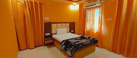 Una habitación de hotel con cama, mesita de noche, aire acondicionado y cortinas.