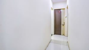 A narrow hallway with white walls and a closed door at the end. - Fabhotel New Shraddha Inn (Nagpur)
