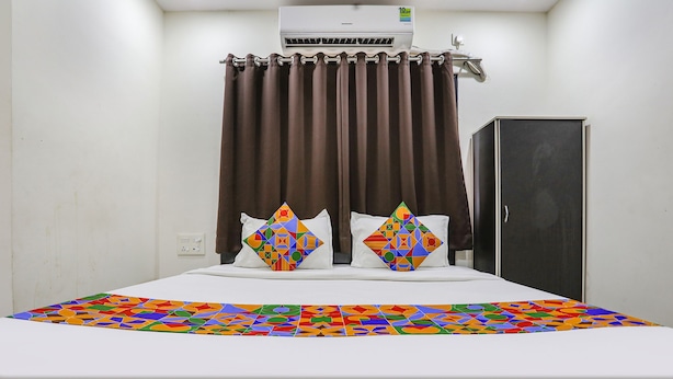 A hotel room with a bed, brown curtains, a wardrobe, and a colorful bedspread. - Fabhotel New Shraddha Inn (Nagpur)