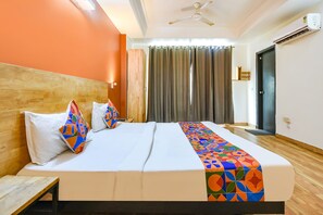 A hotel room with a wooden headboard, a bed with white bedding and colorful pillows, a ceiling fan, and a window with curtains. - FabHotel La Serene NFC (New Delhi)