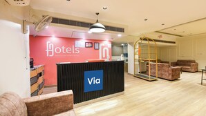 A hotel reception area with a reception desk, a large sign reading 'Hotels India’s First Hybrid Hotels Via,' and a seating area with sofas. - FabHotel La Serene NFC (New Delhi)