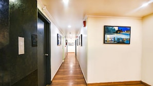 A hallway with wooden flooring, a dark door on the left, and a framed picture on the right wall. - FabHotel La Serene NFC (New Delhi)