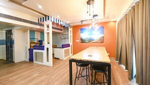 A modern hotel room with a wooden floor, a large dining table, and a kitchen area with a blue and white striped partition. - FabHotel La Serene NFC (New Delhi)