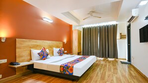 A hotel room with a wooden floor, a bed with a colorful bedspread, a nightstand, a ceiling fan, and an air conditioning unit. - FabHotel La Serene NFC (New Delhi)