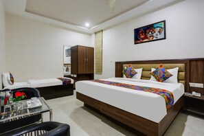 A hotel room with a large bed, a glass table with a chair, a wardrobe, and a painting on the wall.