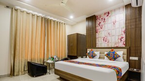 A hotel room with a large bed, a wardrobe, a desk with a chair, and curtains. - Fabhotel Orchid (Agra)