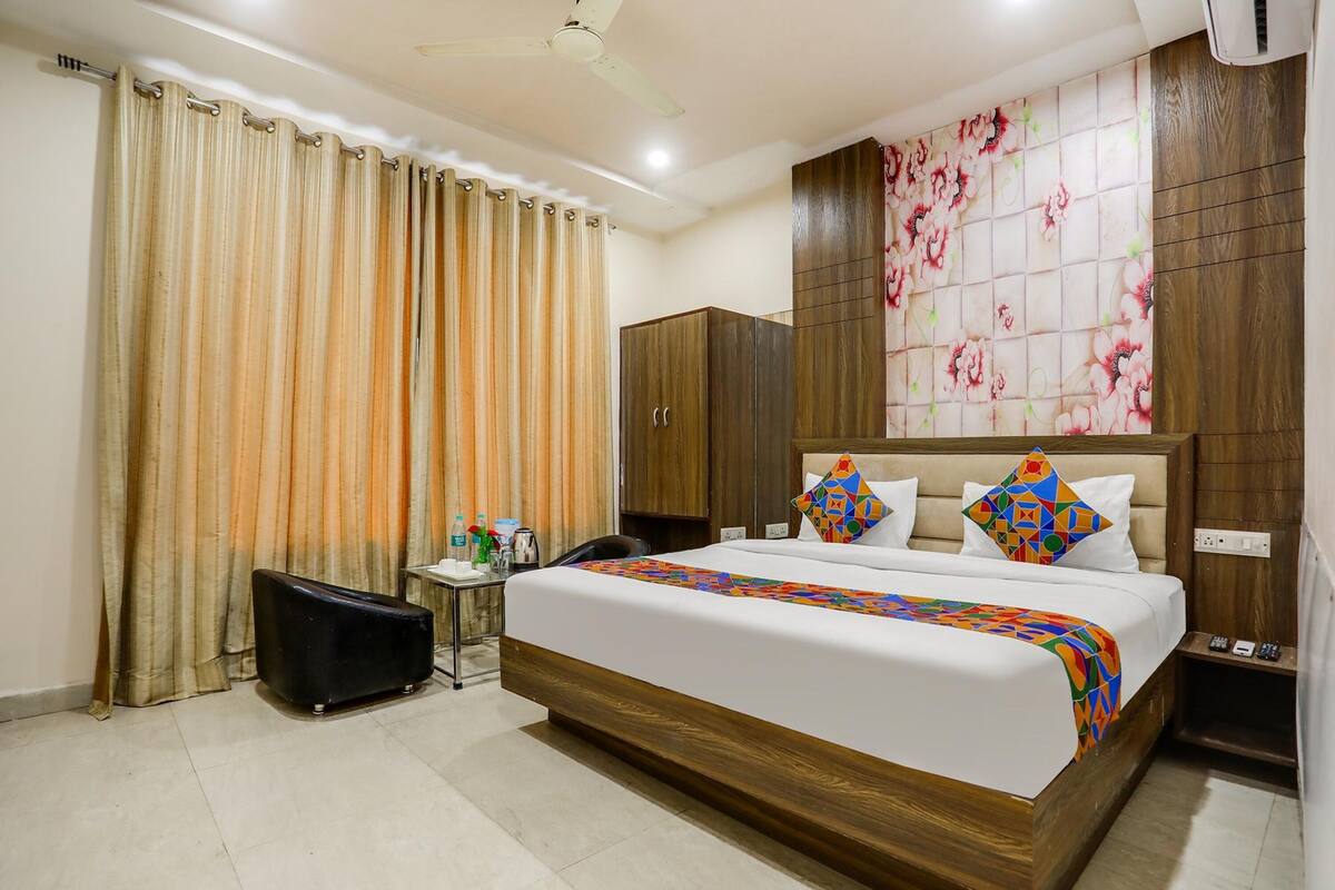 A hotel room with a large bed, a wardrobe, a desk with a chair, and curtains.