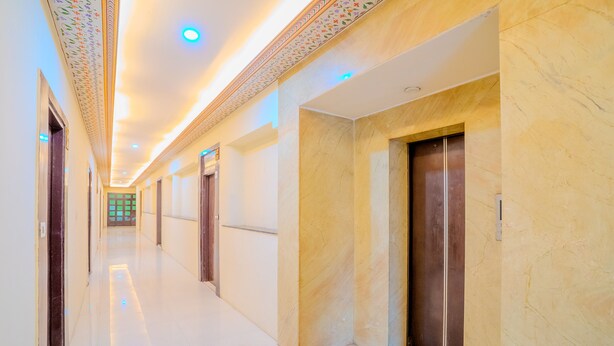A long, well-lit hallway with marble walls and doors, leading to a room with a green view. - Fabhotel Polovictory Palace (Jaipur)