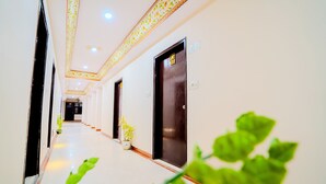 A hotel corridor with a long, narrow layout, featuring doors on both sides, potted plants, and a patterned ceiling design. - Fabhotel Polovictory Palace (Jaipur)