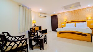 A hotel room with a bed, a desk with a chair, a table, and a ceiling fan. - Fabhotel Polovictory Palace (Jaipur)