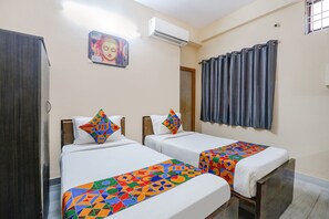 Ein Hotelzimmer mit zwei Betten, einem Schrank, einer Klimaanlage, einem Fenster mit Vorhängen und einem Buddha-Gemälde an der Wand.