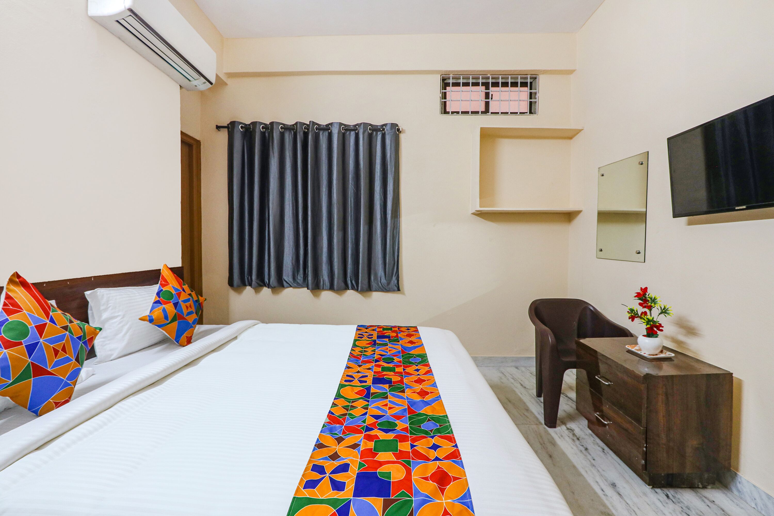 Habitación de hotel con cama, escritorio, silla, televisor y ventana con cortinas.
