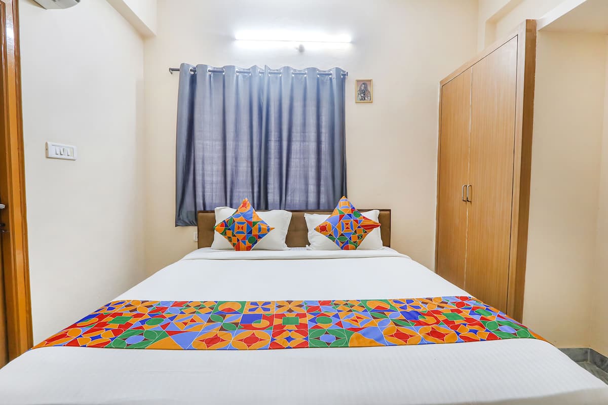 Une chambre d’hôtel avec un lit, un rideau, une armoire et une lampe fixée au mur.