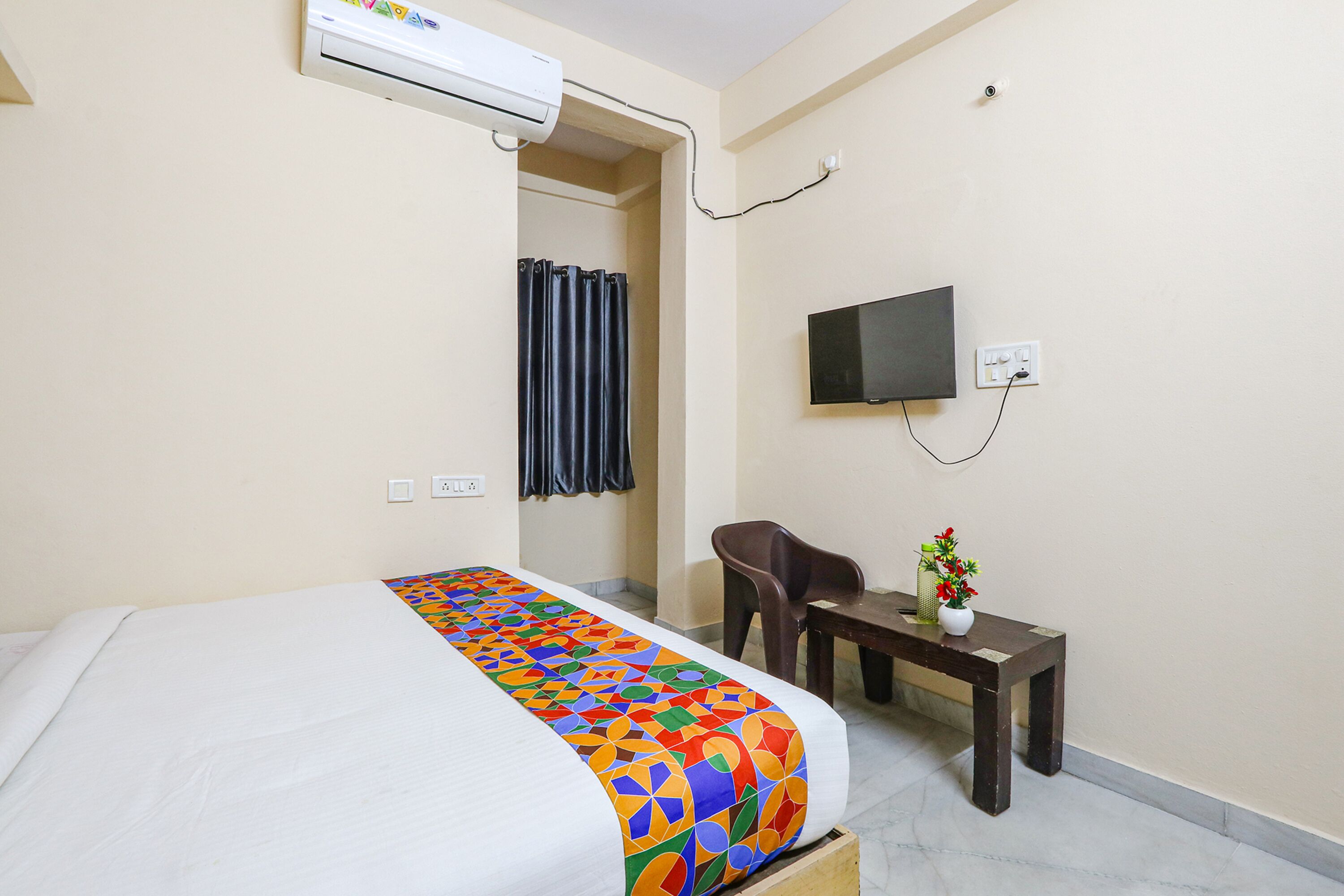 A hotel room with a bed, a desk, a chair, a TV, and an air conditioning unit.