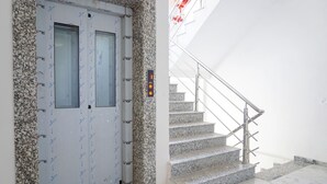 A modern building entrance with a granite-framed door, a stairway with metal railings, and a wall-mounted elevator control panel. - Fabhotel Prime Athiti Delight Stay (Pune)