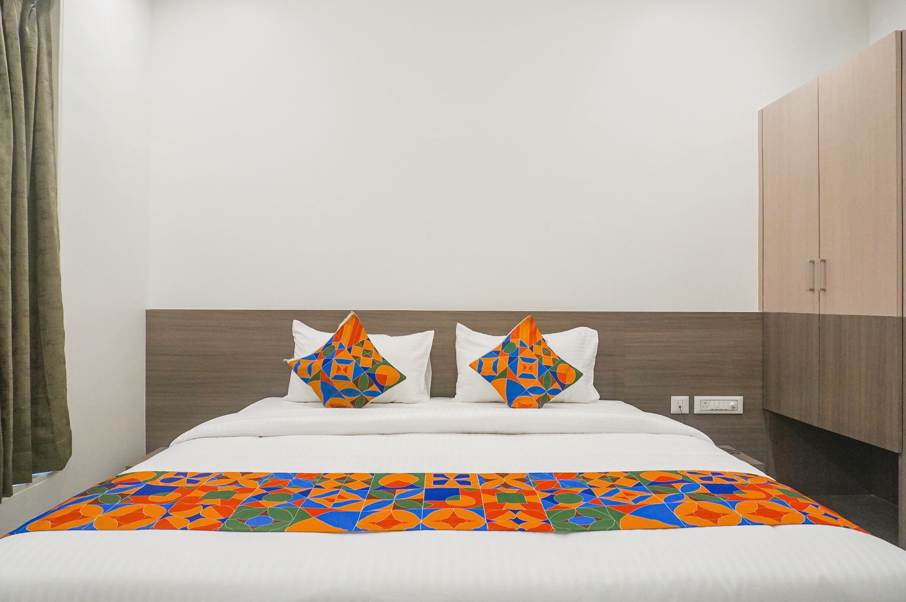 Un lit bien fait, recouvert d’une couvre-lit aux motifs géométriques colorés et agrémenté de deux coussins décoratifs.
