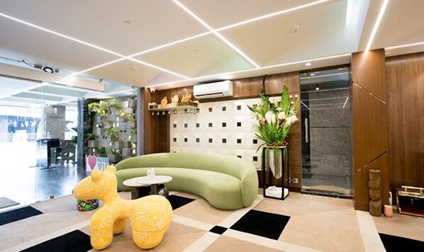 A modern lobby with a green sofa, a yellow plush toy, and a potted plant. - Oriva Vinflora Residency (Hyderabad)