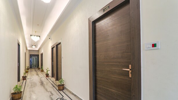 A hallway with marble flooring, potted plants, and wooden doors with a sign above one door. - Fabhotel Raj Palace (Lucknow)