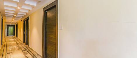 A long, narrow hallway with a marble floor, white walls, and a ceiling with recessed lighting.