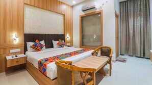 A hotel room with a wooden bed, a desk, and a chair. There is an air conditioning unit on the wall and a window with curtains. - Fabhotel Raj Palace (Lucknow)