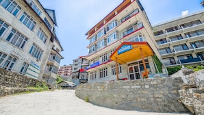 A hotel named "Hotel Sourabh" with multiple floors and balconies, a stone wall in the foreground, and a clear sky. - Fabhotel Saurabh Inn (Manali)