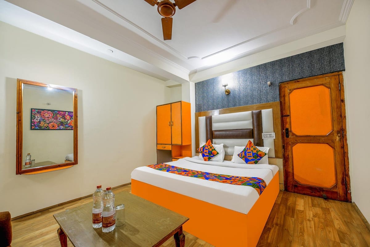 Une chambre d’hôtel avec un lit, une table en bois sur laquelle sont posées des bouteilles, un miroir et une œuvre d’art colorée accrochée au mur.