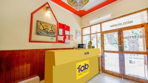 A hotel reception area with a yellow counter, a chandelier, and a large window with a view of the outside. - Fabhotel Saurabh Inn (Manali)