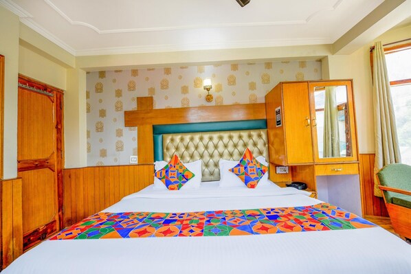 A hotel room with a large bed, a wooden wardrobe, a small desk, and a green armchair.