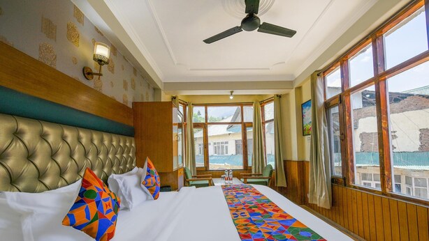 A hotel room with a large bed, a ceiling fan, and large windows offering a view of the outside. - Fabhotel Saurabh Inn (Manali)