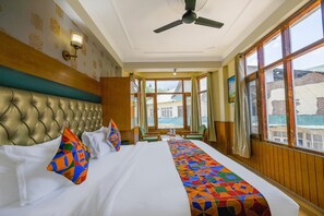 A hotel room with a large bed, a ceiling fan, and large windows offering a view of the outside.