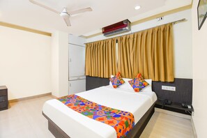 A hotel room with a bed, a bedside table with a phone, a ceiling fan, an air conditioning unit, and a window with curtains.