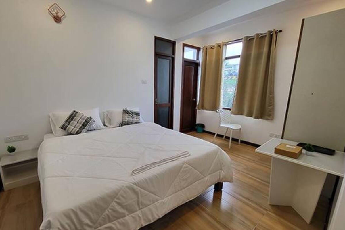 Een slaapkamer met een bed, een stoel, een klein tafeltje en een raam met gordijnen.