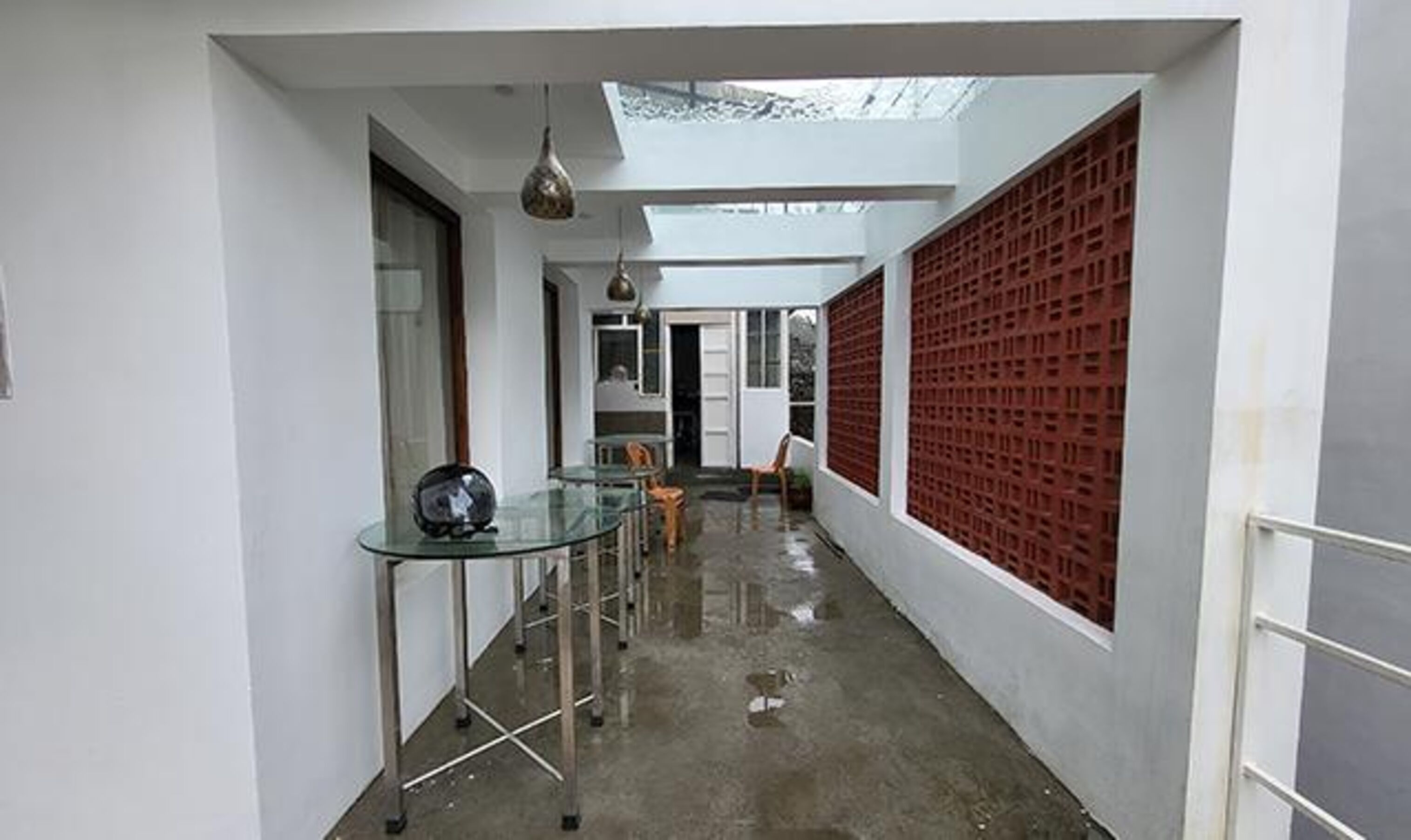 Un couloir étroit avec une table et des chaises en verre, un mur de séparation rouge et une lucarne.