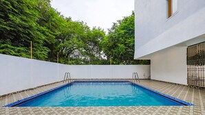 A rectangular swimming pool with a tiled deck, surrounded by a white wall and trees. - Fabhotel Sun Lux Grand Residency (Vanur)