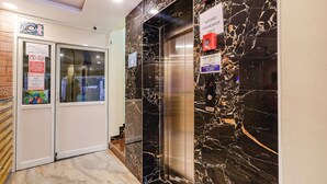 An elevator with a marble wall, a sign indicating it is for passengers only, and a security camera above the door. - Fabhotel Sun Lux Grand Residency (Vanur)