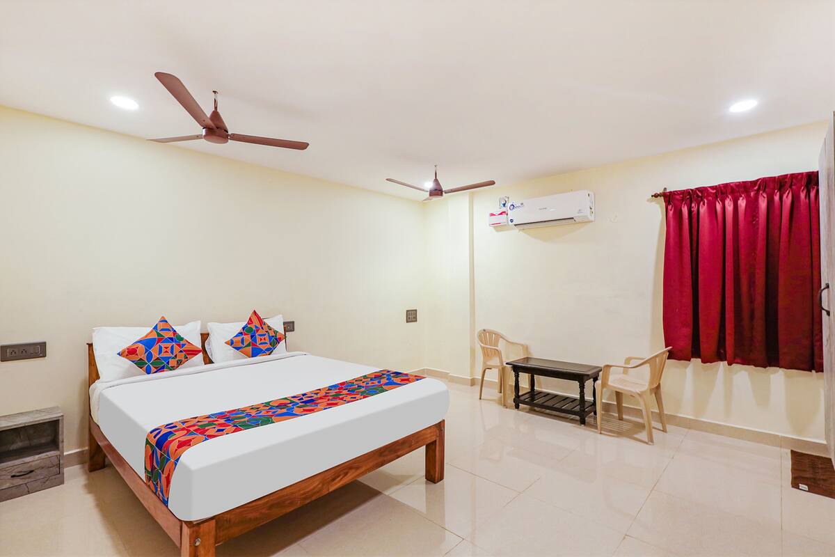 Une chambre à coucher comprenant un lit, deux ventilateurs de plafond, une table, deux chaises, un appareil de climatisation et une fenêtre avec des rideaux rouges.