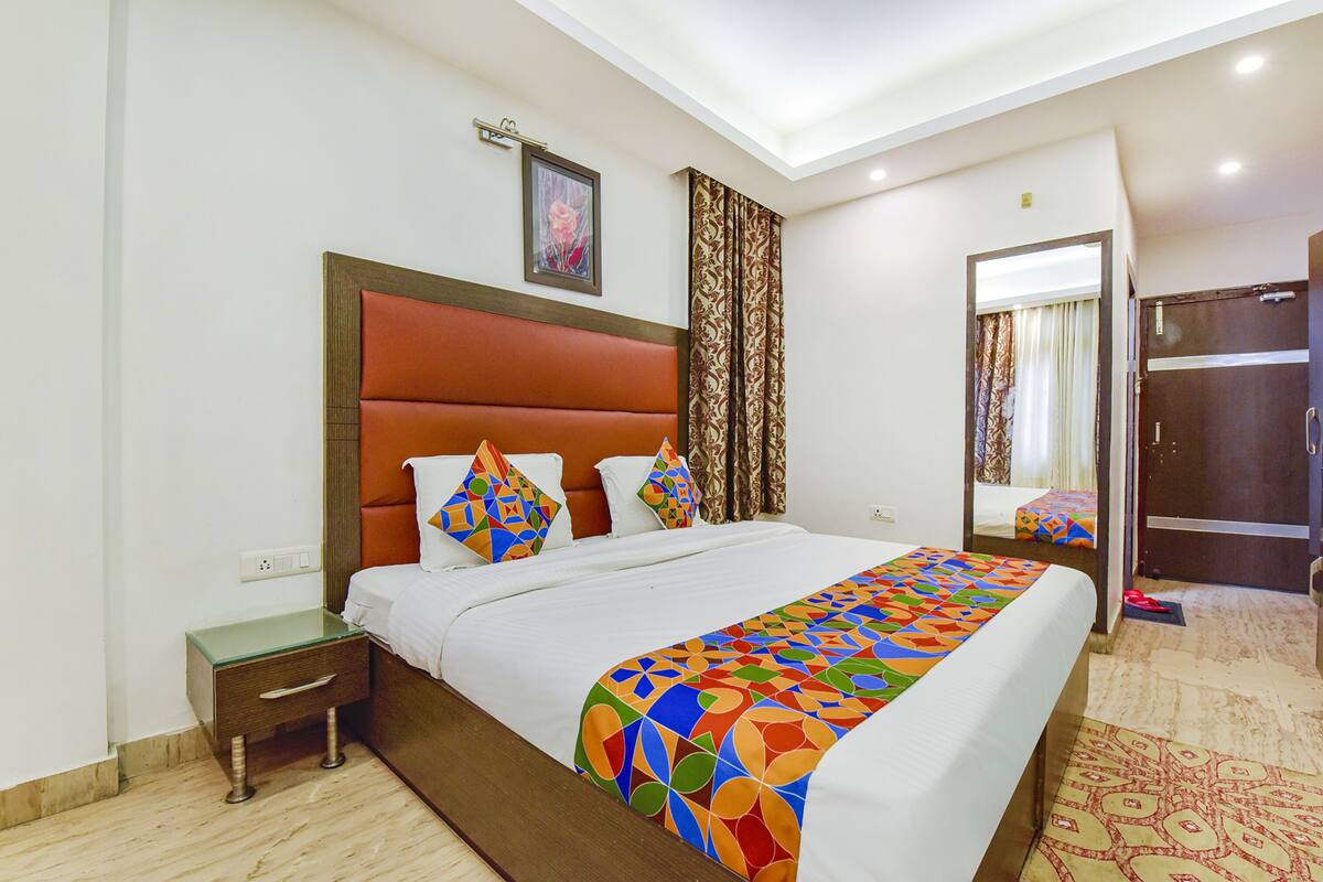 Quarto de hotel com uma cama grande, uma mesa de cabeceira, um espelho e uma porta.
