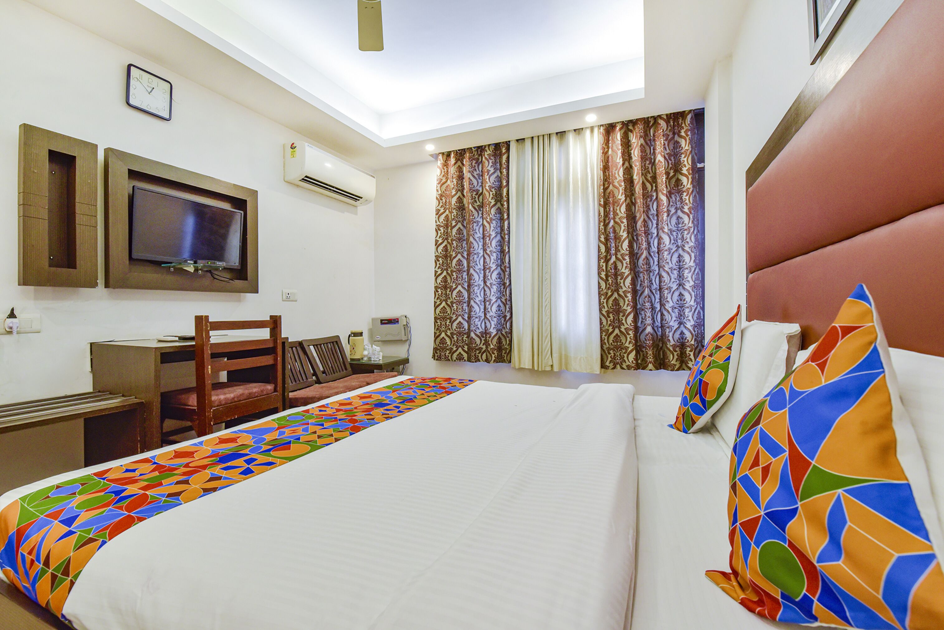 A hotel room with a bed, a desk, a chair, a television, and curtains.