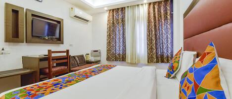 A hotel room with a bed, a desk, a chair, a television, and curtains.
