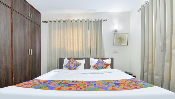 A neatly made bed with a colorful geometric-patterned bedspread, a wooden wardrobe, and a curtain-covered window. - Fabhotel The Legend Residency (Srinagar)