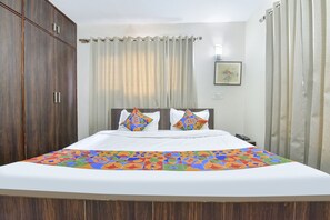A neatly made bed with a colorful geometric-patterned bedspread, a wooden wardrobe, and a curtain-covered window. - Fabhotel The Legend Residency (Srinagar)