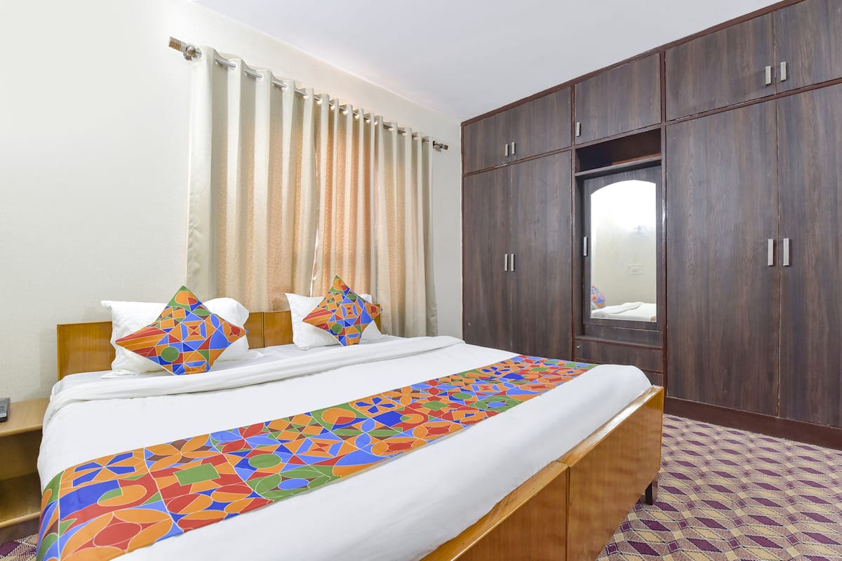 A hotel room with a bed, a wooden wardrobe, a mirror, and a patterned bed runner.